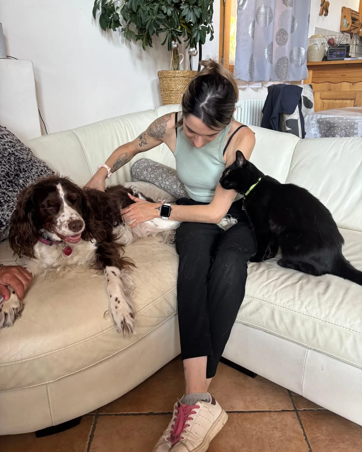 Isabelle Fourcade en séance à domicile, sur un canapé, la main sur le dos d’un épagneul, un chat noir à ses côtés